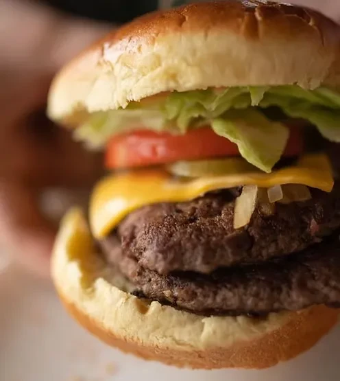 Close-up of a double cheeseburger with melted cheese, lettuce, tomato, pickles.
