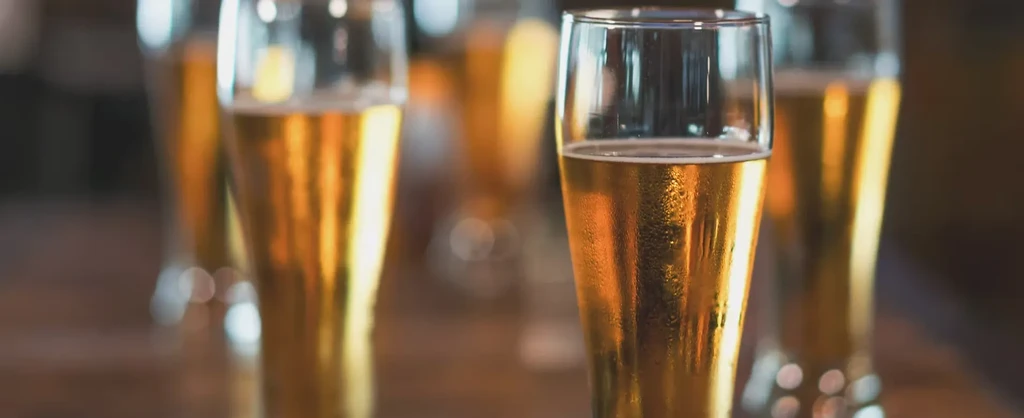 Golden beer glasses with condensation on a warm-lit wooden table.