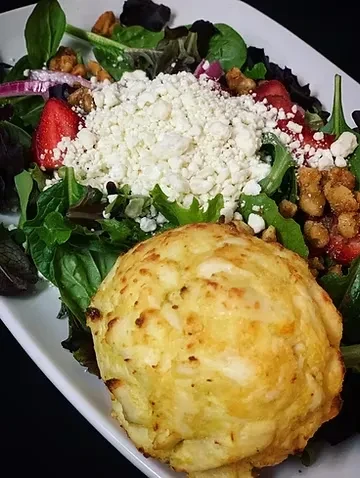 Golden-brown crab cake on salad with feta, strawberries, and walnuts.