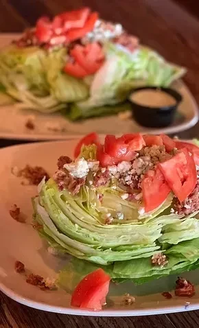 Two crisp wedge salads with blue cheese, bacon, and tomatoes.