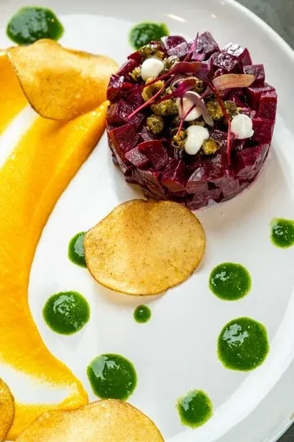 Plated gourmet beet stack with orange purée, green oil, and chips.