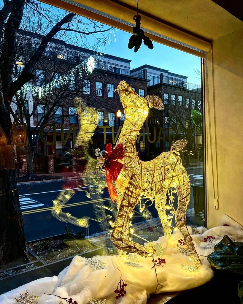 Golden reindeer decoration in a festive window display with urban street background.