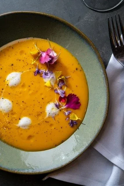 Creamy orange soup in a rustic bowl, garnished with flowers and spice.