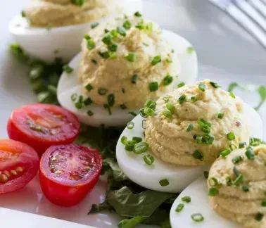 Deviled eggs with chives, cherry tomatoes, and greens on a white plate.