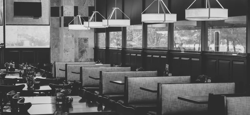 Empty black and white restaurant interior with booths, tables, and windows.