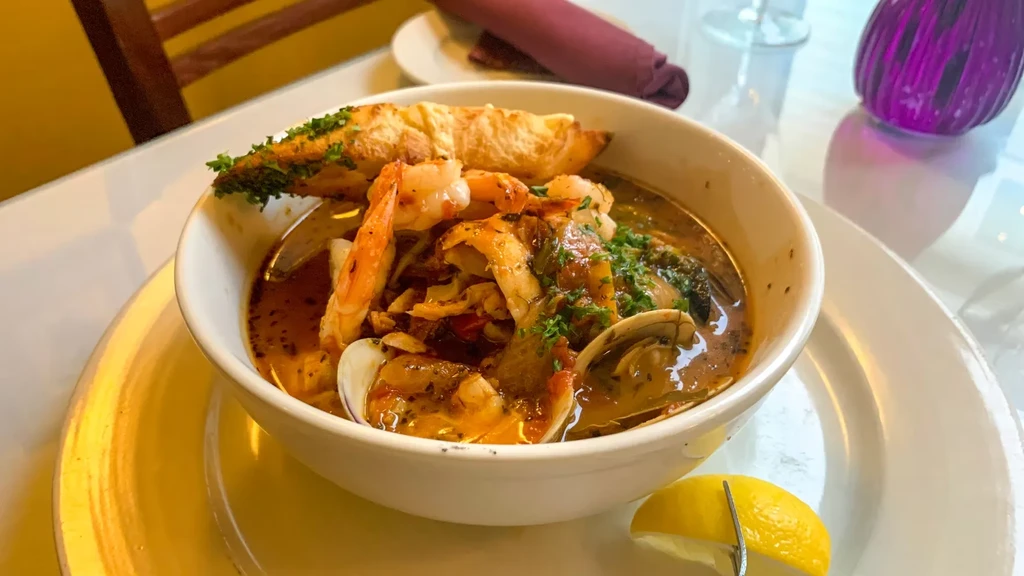 Close-up of seafood stew with shrimp, clams, crusty bread, lemon.