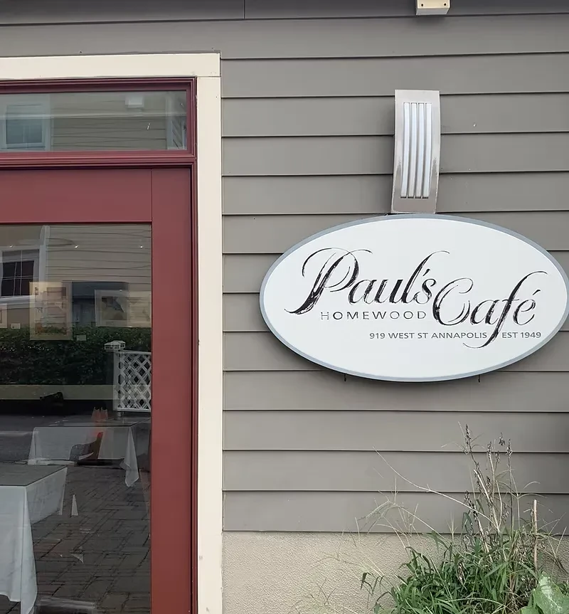 Oval white sign for Pauls Cafe Homewood on a grey building.