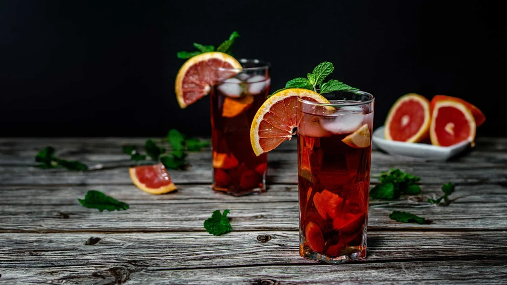 Two red grapefruit drinks garnished with mint on wood.