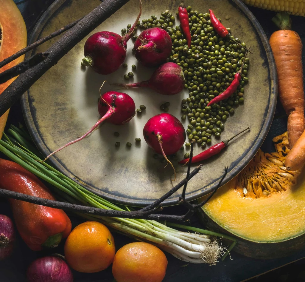 Vibrant assortment of raw fruits and vegetables on and around a plate.