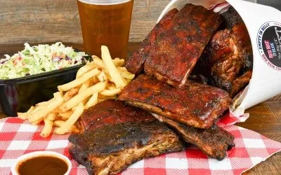 BBQ ribs, fries, coleslaw, and dipping sauce on a wooden surface.