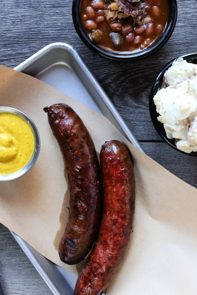 Grilled sausages, mustard, baked beans, and potato salad meal.