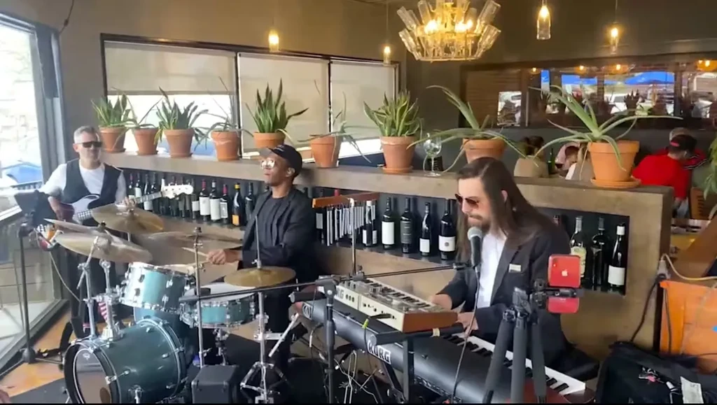 Three musicians play live in a restaurant with bottle chandelier.