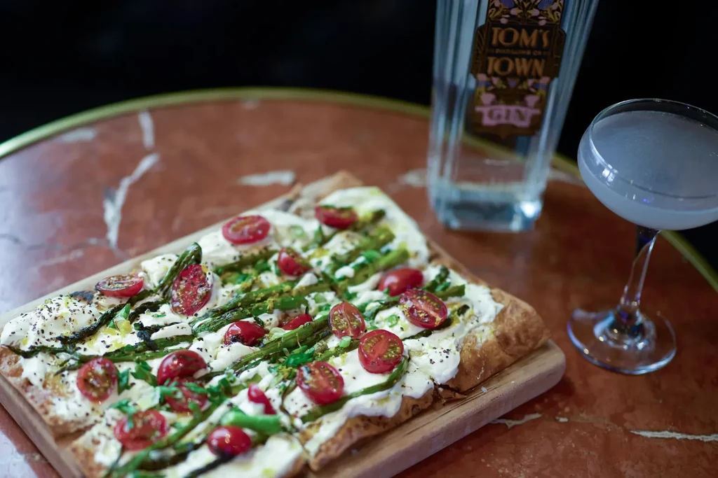 Cheesy flatbread with tomatoes, asparagus; gin bottle and cocktail.