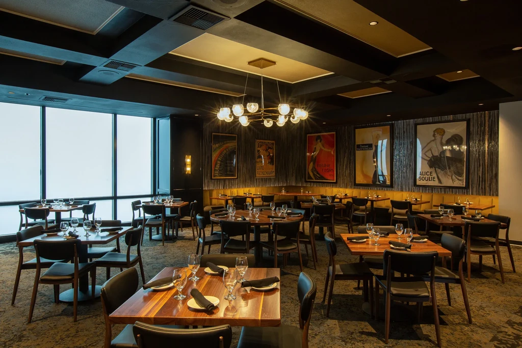 Modern upscale restaurant dining room, empty with set wooden tables.