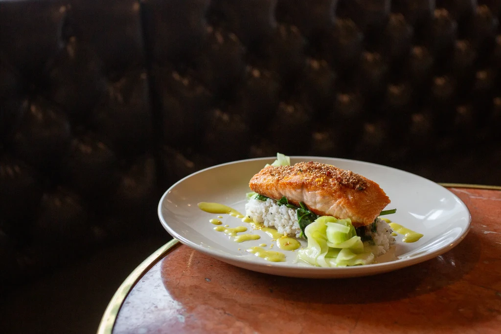 Plated golden-brown fish, rice, greens, and sauce on a marble table.