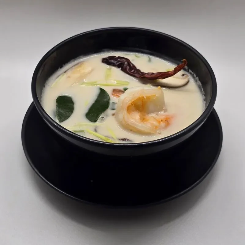Close-up of creamy Thai coconut soup with shrimp, lime leaves, chili.