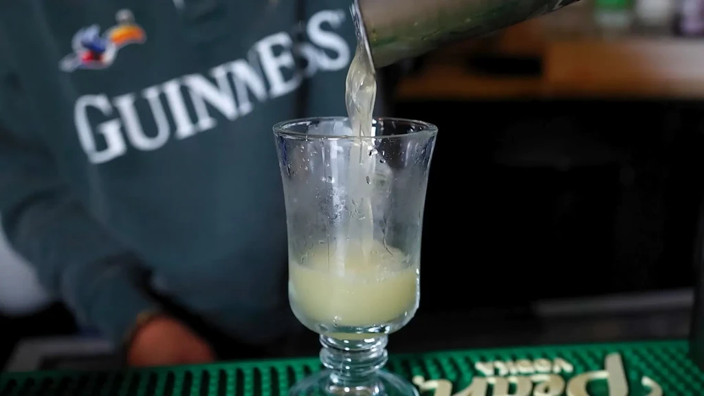 Light yellow drink pouring into a frosted stemmed glass.