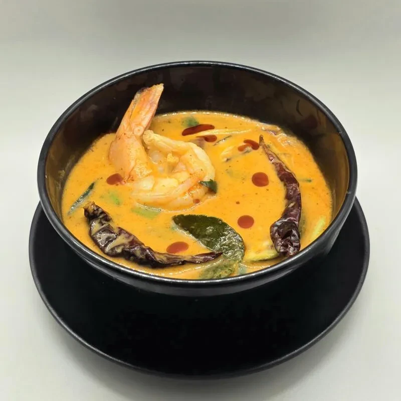 Vibrant orange shrimp curry in a black bowl with green garnishes.