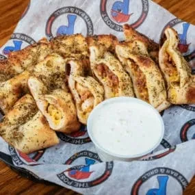 Golden-brown dough bites with herbs and dipping sauce in a branded basket.
