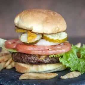 Stacked hamburger with cheese, vegetables, and golden-brown french fries.
