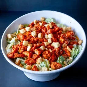 White bowl of salad with reddish-orange chicken and croutons.