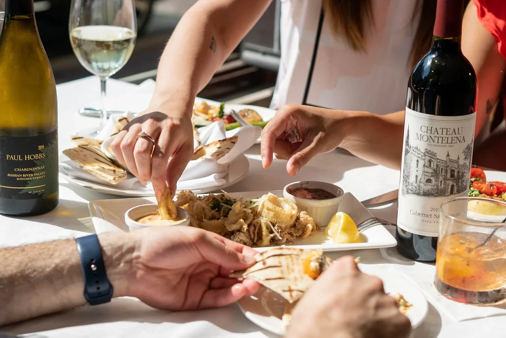 Close-up of hands sharing fried calamari, flatbread, white and red wine.