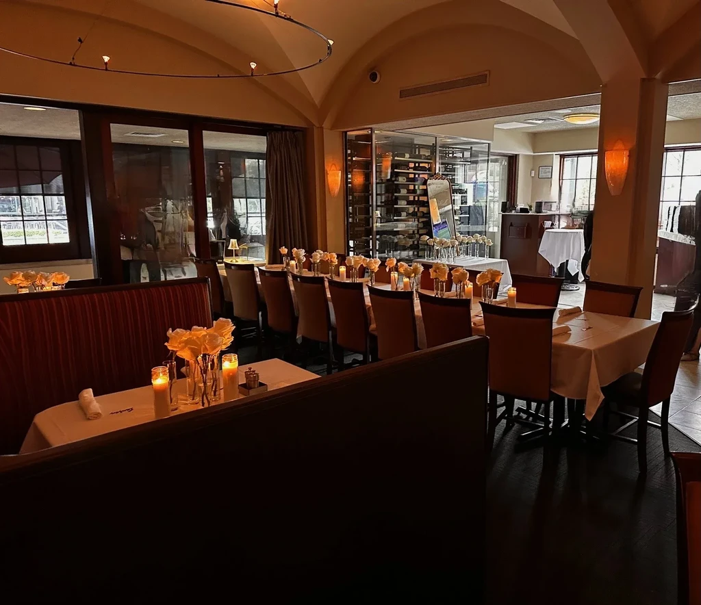 Elegant restaurant dining area with set tables, flowers, candles, and wine cellar.