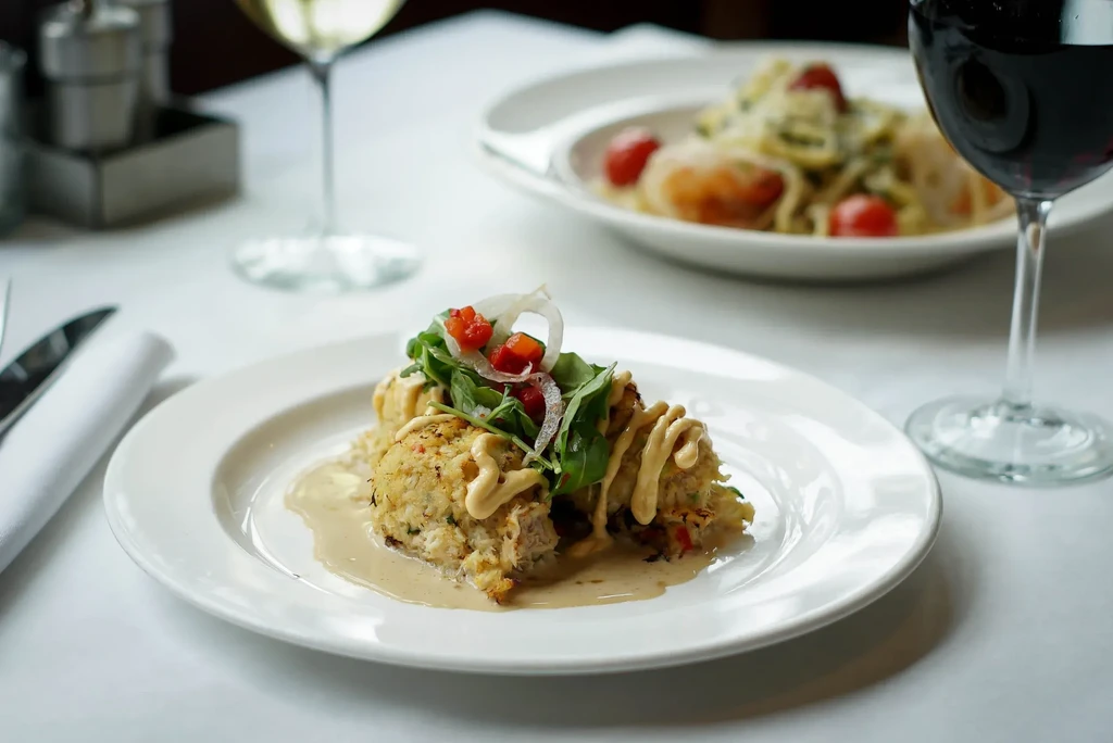 Close-up of crab cakes with sauce, greens, onions, and tomatoes.