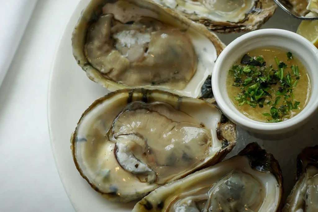 Fresh oysters on a white plate with sauce and lemon.