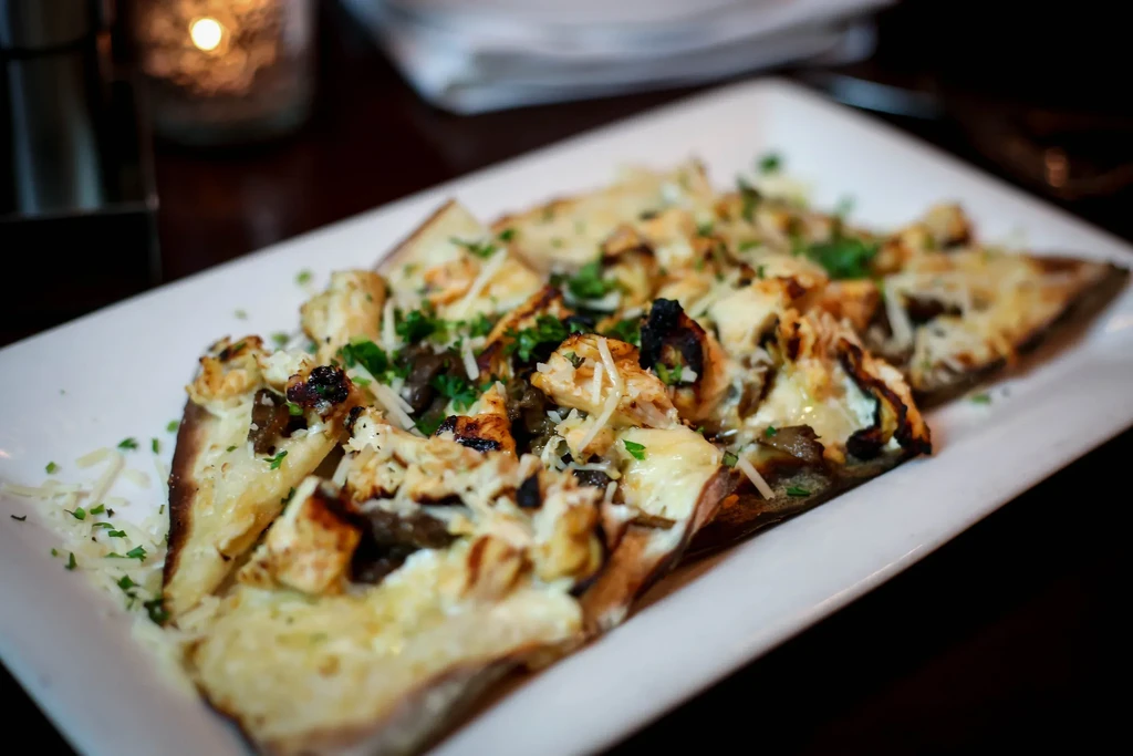 Grilled chicken flatbread with melted cheese and parsley on a white plate.
