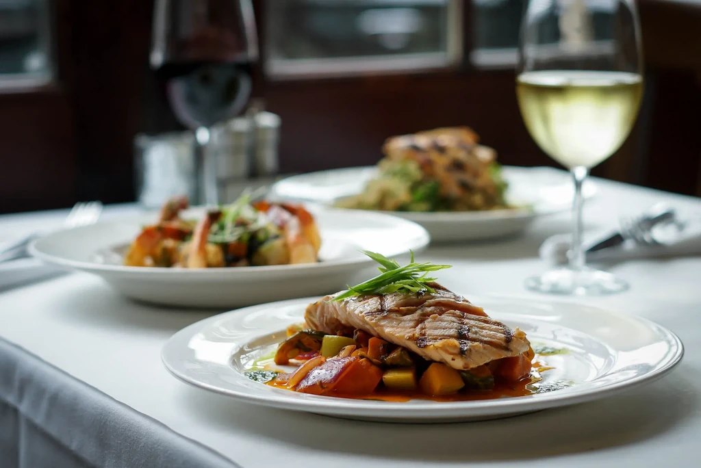 Elegantly plated grilled fish, other dishes, and wine on a restaurant table.