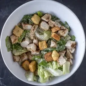 White bowl filled with Caesar salad, chicken, and croutons.