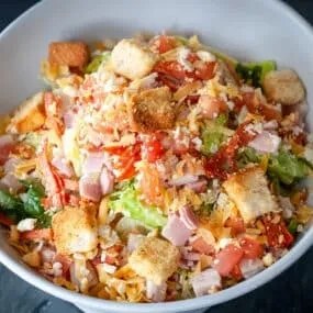 Generously portioned salad with lettuce, ham, cheese, tomatoes, and croutons.