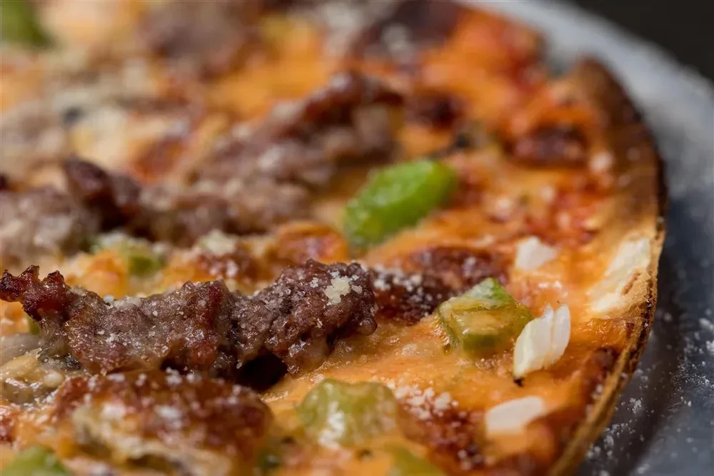 Close-up pizza with browned meat, green peppers, and melted cheese.