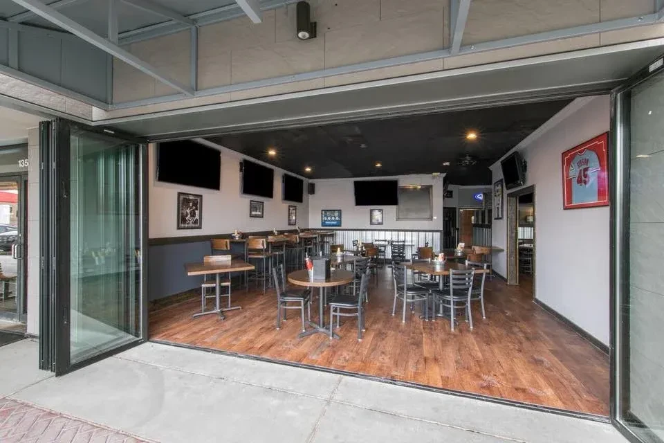 Open-air sports bar interior with TVs, sports jerseys, dark wood furniture.