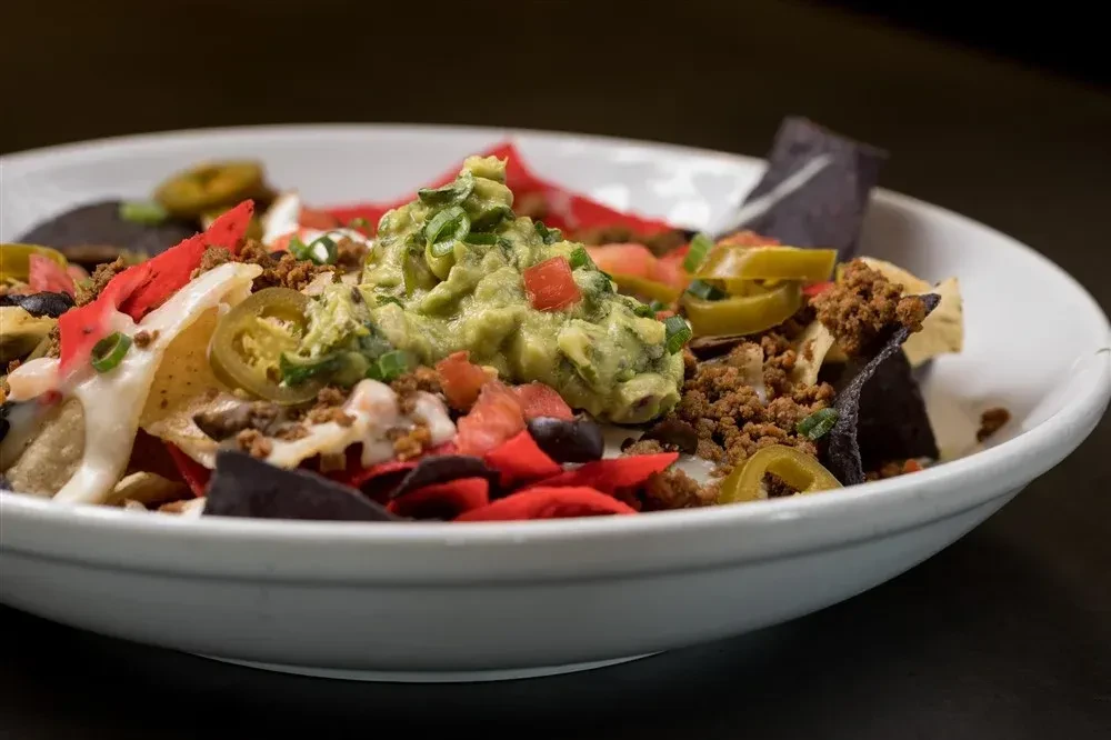 Mixed tortilla chip nachos with meat, cheese, jalapeños, and guacamole.