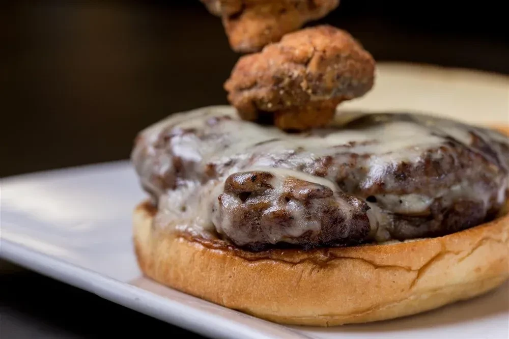 Beef burger with melted white cheese and crispy fried mushrooms on a bun.