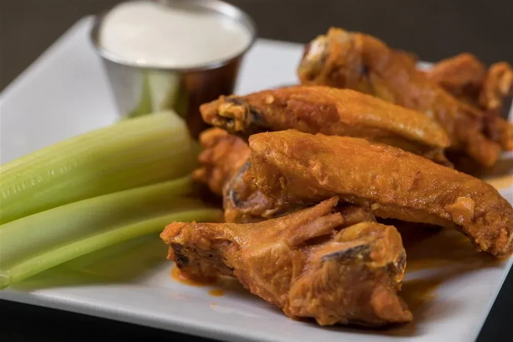 Golden-brown chicken wings with celery sticks and creamy dipping sauce.