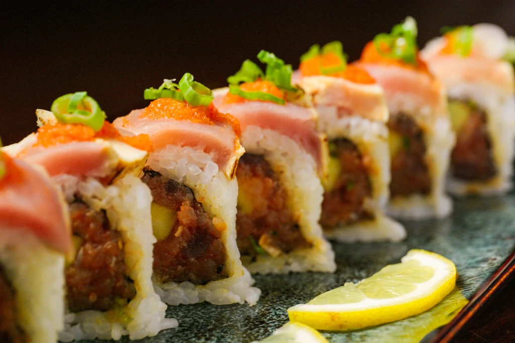 Close-up of colorful sushi rolls with fish, roe, onions, and lemon.