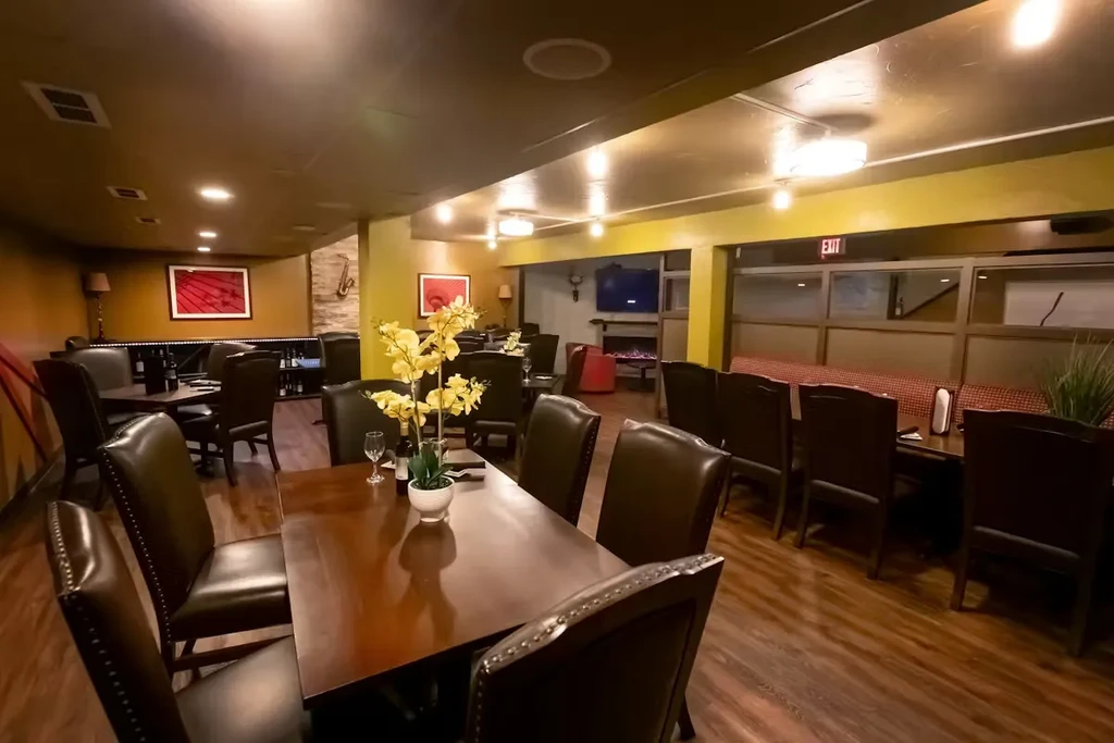 Warmly lit, empty restaurant interior with tables, artwork, and a saxophone.