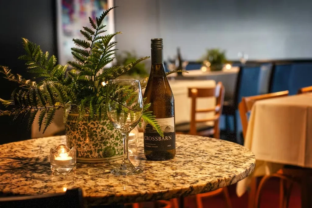 Restaurant table with Crossbarn Chardonnay, lit candle, and potted fern.