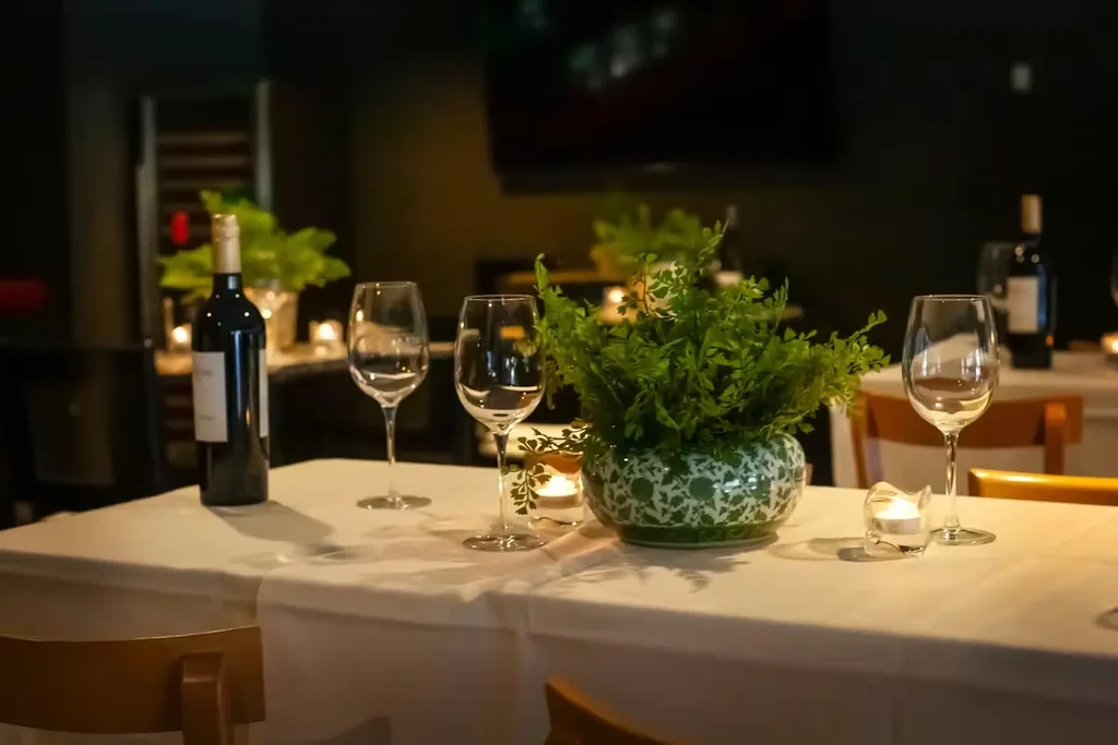 Upscale restaurant table with wine bottle, plant, glasses, and lit candles.