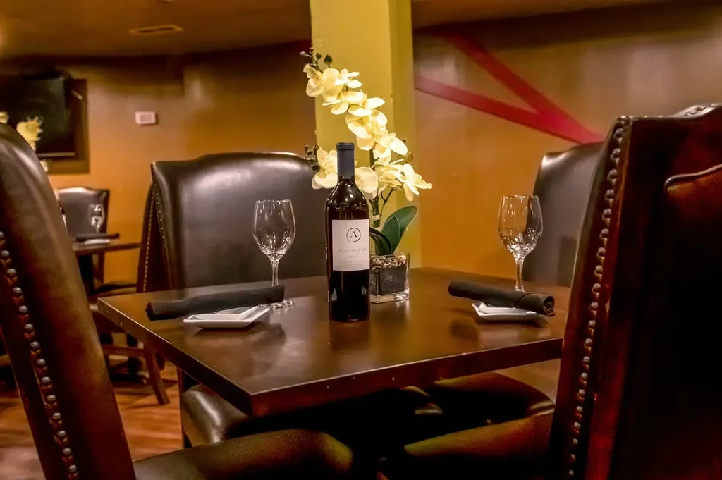 Restaurant table set for two with red wine, label 'ADAPTATION', and orchid.