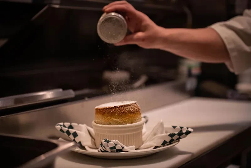 Risen golden-brown soufflé in ramekin, dusted with powdered sugar.