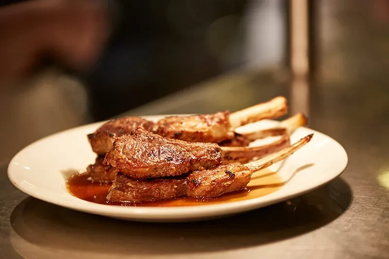 Grilled lamb chops with sauce and visible grill marks on plate.