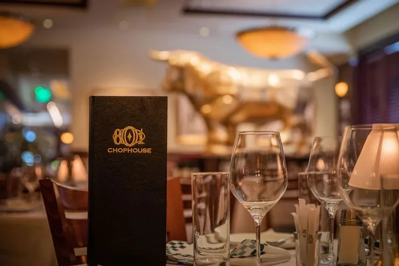 Restaurant table with '801 CHOPHOUSE' menu, glassware, and golden bull sculpture.