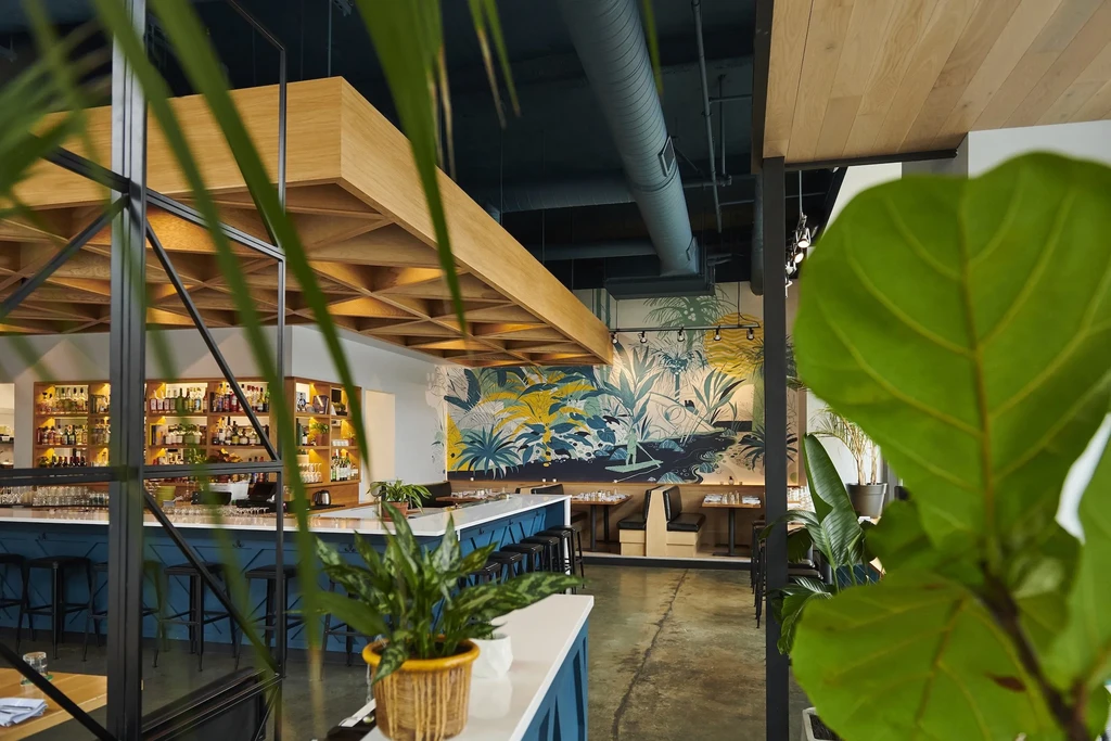 Industrial-chic bar and restaurant with plants and a jungle mural.