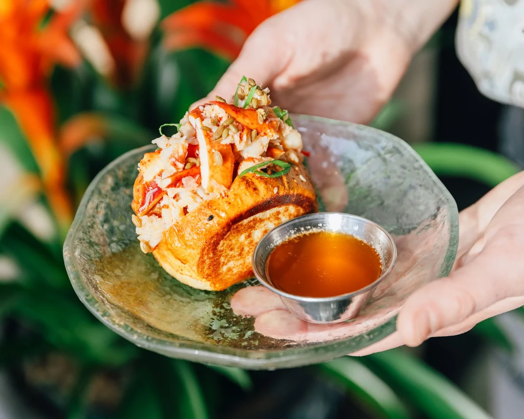 Close-up of a lobster roll with herbs and butter, held outdoors.