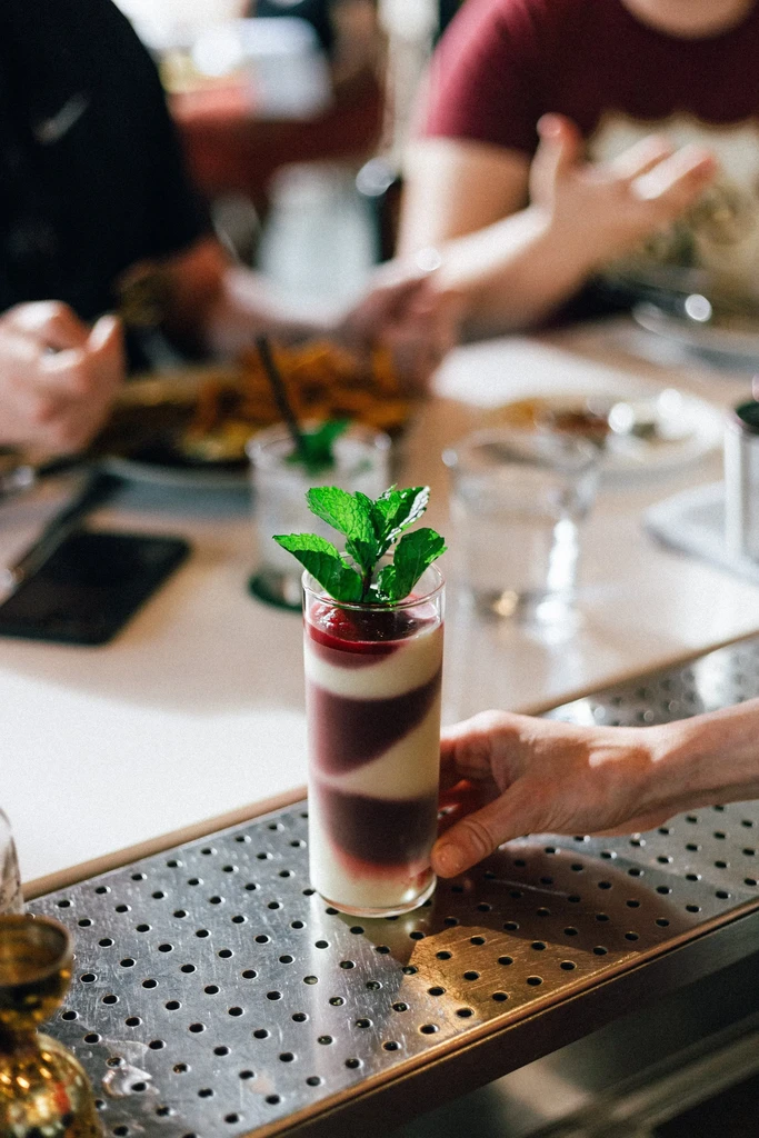 Hand holds a layered red, purple, and white dessert glass with mint.