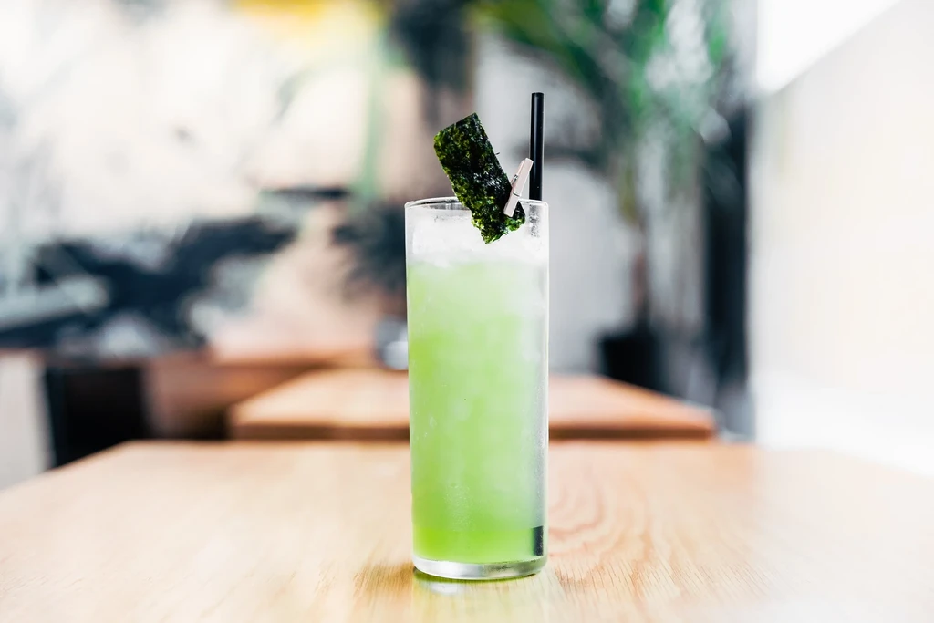 Green beverage with ice, black straw, and seaweed garnish.